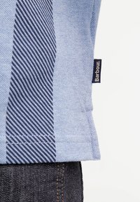 Chemise bleu clair avec des rayures diagonales bleu foncé, en tissu texturé, et une petite étiquette bleue avec "Barbour" à l'ourlet.