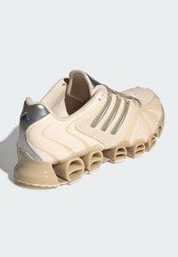 Béžová športová obuv s mesh vrchnou časťou, striebornými doplnkami a výrazným tubulárnym dizajnom podrážky. Disponuje šnúrkami a tromi pruhovanými prekrytiami.