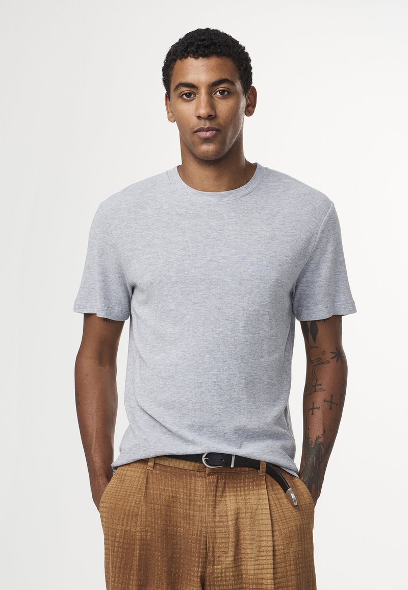 Lys grå kortærmet t-shirt med rund hals, lavet af blødt stof, parret med brune teksturerede bukser og et sort bælte.