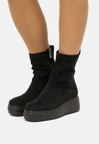 Bottines en daim noir avec un design décontracté, dotées d'une fermeture éclair sur le côté et d'une semelle épaisse et texturée pour une meilleure adhérence.