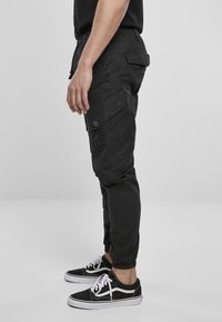 Pantalones cargo negros con puños elásticos, múltiples bolsillos laterales y un ajuste relajado, combinados con zapatillas negras con acentos blancos.