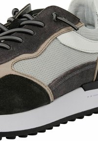 Sneaker aus einer Mischung von grauem Wildleder und Mesh-Materialien, mit einem weißen Lederakzent und einer dicken schwarzen Gummisohle mit strukturiertem Grip.