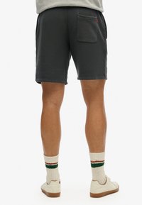 Katoenen shorts in donkergrijs met een achterzak en een rode logo patch, gecombineerd met witte sneakers en gestreepte sokken.