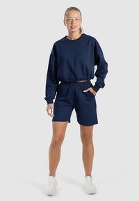 Diepblauwe trui met een ronde hals en elastische zoom; gecombineerd met bijpassende korte broek met een elastische tailleband en zijzakken.