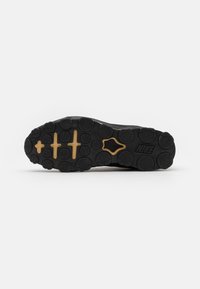 Sola de sapatilha preta com padrões de adesão circulares, pinos hexagonais e um detalhe em dourado com a marca "NIKE". Construção em borracha durável.