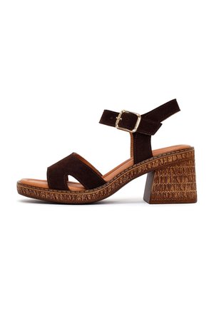 Sandale marron en daim à bout ouvert avec un motif découpé, bride de cheville réglable à boucle dorée et talon bloc texturé.