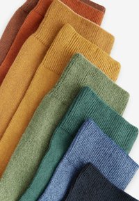 Volnene nogavice v gradientu barv: rjača, rumena, zelena, modra in mornarsko modra. Vsaka nogavica ima rebrasto teksturo in različne dolžine.