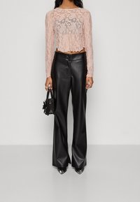 Ljusrosa spetscroppad topp med långa ärmar, kombinerad med högmidjade svarta läderbyxor med vida ben. Liten svart handväska med blommig detalj.