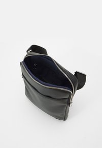 Melnas ādas crossbody soma ar gludu tekstūru, sudraba rāvējslēdzis un vienu ārējo kabatu. Iekšpusē izklāta ar zilu audumu.