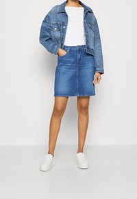 Jeansjacka och vit T-shirt kombinerat med en blåjeanskjol som har en figurnära passform, ljus tvätt och sidofickor, avslutat med vita slip-on skor.