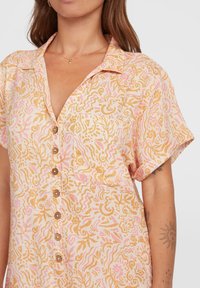 Chemise à manches courtes en tissu léger avec un motif tourbillonnant rose et or. Comprend un col et des boutons en bois sur le devant.