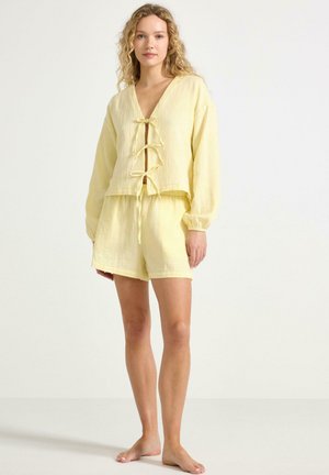 Gul lin loungewear-set bestående av en kortad topp med V-ringning och knytningar, som matchas med shorts, båda med en texturerad yta.