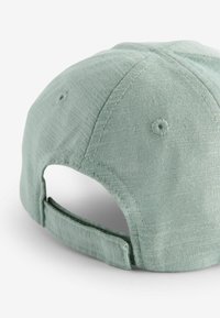 Gorra de algodón verde claro con un acabado texturizado, que cuenta con una correa ajustable en la parte posterior y agujeros de ventilación cosidos en la parte superior.