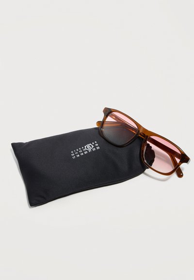 Καφέ γυαλιά με ροζ φακούς που ακουμπούν σε μια μαύρη μαλακή θήκη με εκτυπωμένες λευκές κυκλικές ημερομηνίες και αριθμούς.