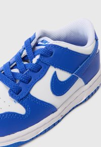 Modré a biele Nike tenisky vyrobené z kože a sieťoviny, s polstrovaným golierom, perforovanou špičkou a textúrovanou gumovou podrážkou.