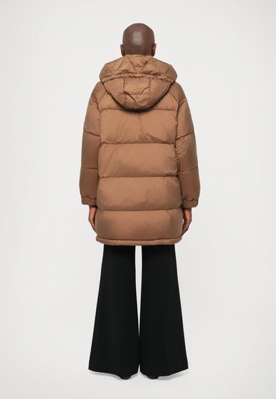 Casaco puffer castanho com capuz, apresentando um detalhe acolchoado. Usado sobre calças largas pretas, enfatizando um corte descontraído.