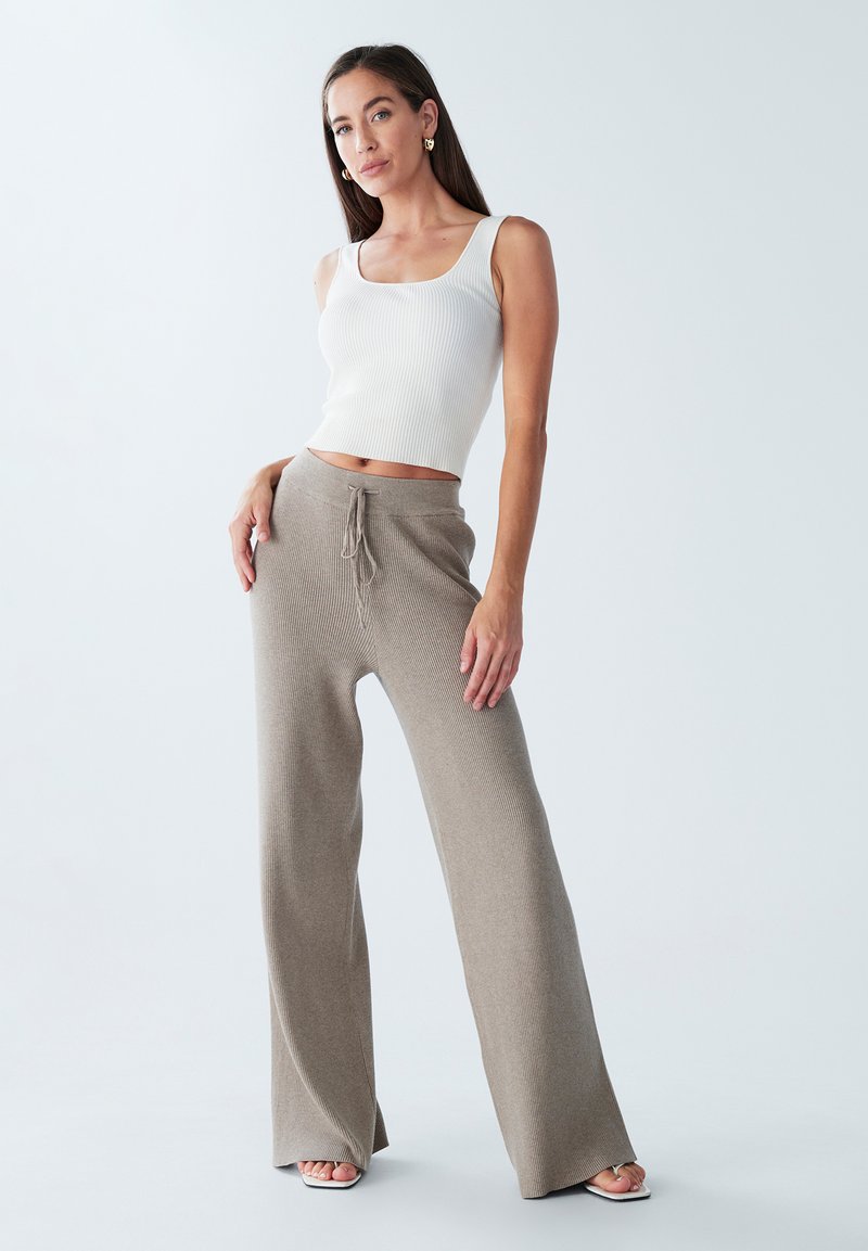 Top corto bianco a coste con scollatura quadrata abbinato a pantaloni beige a gamba larga con vita regolabile, entrambi realizzati in un tessuto morbido e testurizzato.