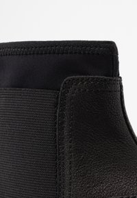 Černé kotníkové boty s hladkou koženou částí a textilním svrškem, s prošitým švem podél okraje a elastickým límcem.