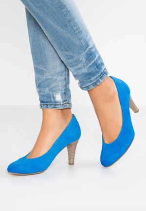 Blauwe suède high heels met een ronde neus, voorzien van een gestructureerde, lichtbruine kegelvormige hak. Draagt bij lichte blauwe distressed jeans.