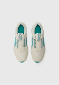 Nike Sneaker mit einem hellbeigen Obermaterial, kombiniert mit türkisfarbenen Akzenten, Netzstruktur und Schnürdesign. Das Markenlogo ist sichtbar.