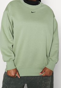 Ljusgrön sweatshirt med rund halsringning, ribbade muddarna och en liten svart Nike-logotyp på bröstet. Mjuk tyg med en avslappnad passform.