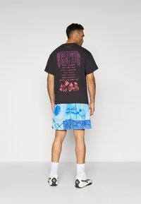 Svart T-skjorte med rosa grafisk tekst p�å baksiden, kombinert med blå mønstrede shorts med basketball-design, hvite sokker og sneakers.