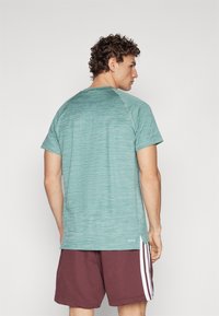 Short-sleeve teal athletic shirt with a textured pattern, raglan sleeves, and a side slit, paired with maroon shorts featuring white stripes.