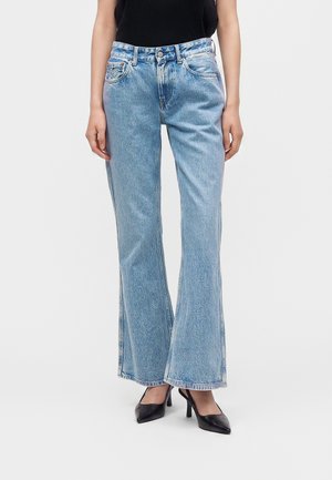 Femme portant un jean bleu clair taille haute à jambes droites, associé à des talons hauts noirs à bouts pointus et un haut noir.