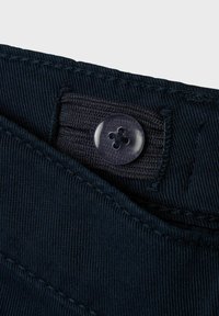 Tissu en velours côtelé bleu marine avec un bouton en plastique visible présentant un motif de fleur et des accents cousus à la taille.