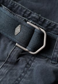 Mørkeblå tekstilbælte med en struktureret overflade, metalspænde og accentstykke, der fremviser syninger og et vævet udseende.