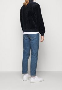 Black, textured bomber jacket with a high collar, paired with light blue, straight-leg jeans and white sneakers. Minimalist design.