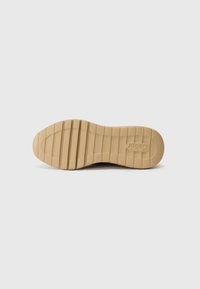 Semelle de chaussure en caoutchouc beige avec un motif nervuré et un logo imprimé. Présente un design plat avec des rainures pour l'adhérence et la stabilité.