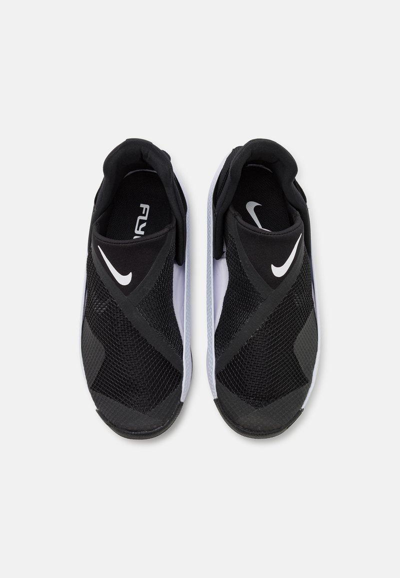 Zapatillas Nike slip-on en blanco y negro con paneles de malla, una suela texturizada y un diseño curvo prominente con un logo blanco.