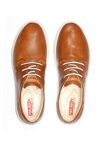 Zapatos de cuero marrón con un acabado texturizado, cordones blancos y plantilla beige. Presentan una puntera redonda y suela de goma blanca.