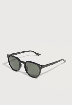 Lunettes de soleil Gucci noires avec verres foncés, logo de marque doré et petits accents dorés sur les coins avant et les branches.