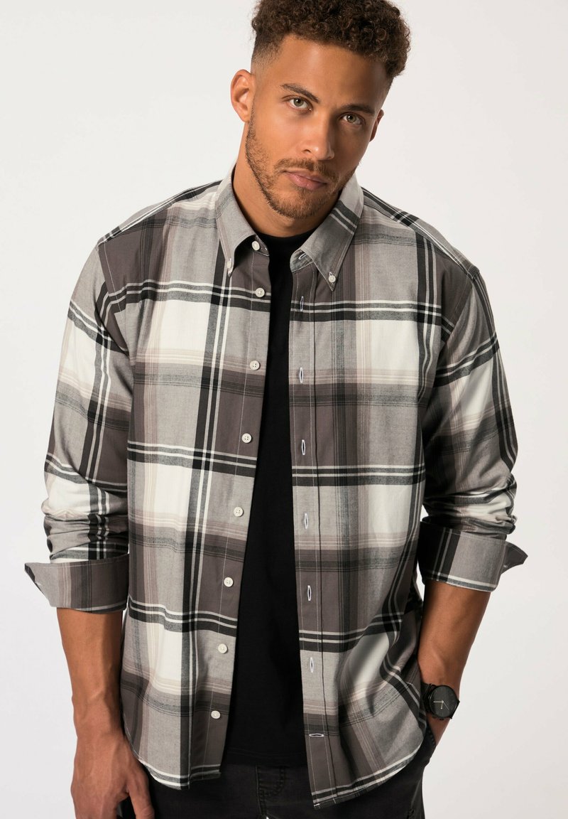 Camicia a scacchi grigia e nera con maniche arrotolate, strisce bianche a contrasto e una maglietta nera sotto. Presenta bottoni visibili e colletto.
