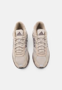 Beiga sportskor med ett nätövre, texturerade detaljer och skosnören. Tre gråaktiga ränder på sidorna, gummisula.