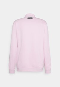 Světle růžová mikina s dlouhými rukávy z pohledu zezadu, s malou černobílou nášivkou loga Adidas blízko límce.