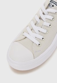 Beige canvas sneakers med hvite snøringer, gummitåhette og metalløyelister. Har subtile stikkingdetaljer og en teksturert gummisåle.