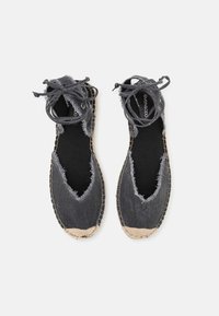 Coppia di espadrillas in denim nero con bordi sfrangiati, suole beige cucite e lacci avvolgenti alla caviglia su sfondo bianco.