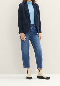 Marineblauer, gestreifter Blazer über einem hellblauen Rollkragenpullover, kombiniert mit lockeren blauen Jeans und cremfarbenen Stiefeletten mit schwarzen Sohlen und Reißverschlüssen.