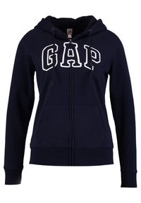 Sweat à capuche zippé bleu marine avec logo "GAP" blanc, capuche avec cordon de serrage, poches avant et poignets côtelés. Fabriqué en matière douce mélange de coton.
