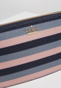 Striped cosmetic case featuring navy, light blue, and pink colors with a glittery finish; includes a gold-tone logo and zipper.