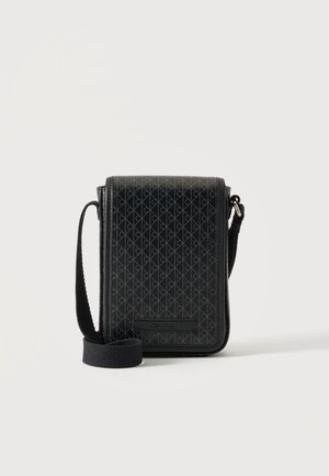 Petit sac bandoulière noir avec motif géométrique, sangle ajustable et fermeture à rabat, debout sur un fond clair.