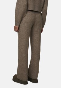 Brązowe, teksturowane, szerokie spodnie dzianinowe z rypsowym paskiem i mankietami, w połączeniu z ciemnym obuwiem. Miękki, przytulny materiał o swobodnym kroju.
