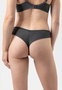 Zwarte onderbroek van een gladde, rekbare stof, met een lage taille en minimale bedekking, gezien vanuit een achteraanzicht.