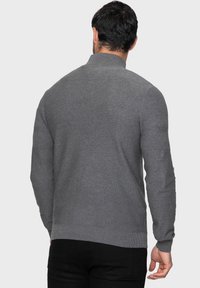 Suéter gris con un cuello alto, puños acanalados y acentos texturizados en los hombros. Hecho de material suave, diseñado para un ajuste cómodo.
