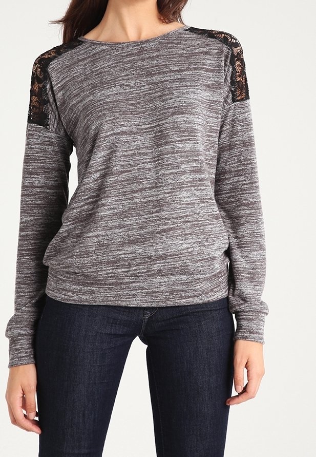 Maglia grigia a maniche lunghe in tessuto testurizzato, con motivo a righe e dettagli in pizzo nero sulle spalle. Abbinata a jeans scuri.