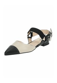 Zapato de punta con una parte superior de cuero crema y negro, que presenta una correa de tela negra en el tobillo y un herraje plateado ajustable. Tacón bajo tipo bloque.