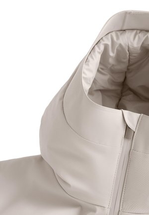 Jachetă bej deschis cu glugă, o parte exterioară netedă, impermeabilă, fermoar vizibil și căptușeală interioară moale și căptușită.